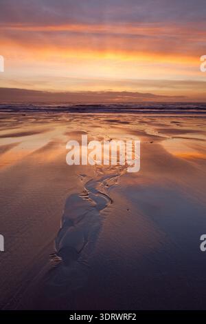 Twilight stream cutting across a wide sandy beach beneath dramatic clouds in Wales. Stock Photo