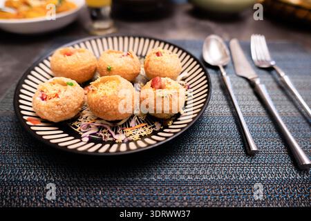 Indian Pani Puri Snack on Black Plate with Garnish, Served with Silver Cutlery on Textured Tablecloth Stock Photo