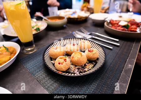 Indian Pani Puri snacks on patterned plate with drinks and side dishes at restaurant table Stock Photo