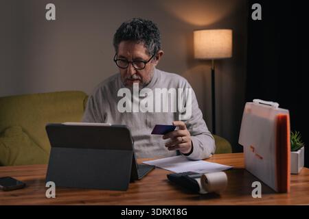 Middle aged man at home using tablet and credit card to pay bills online. Concept of digital banking, personal finance management and online transacti Stock Photo