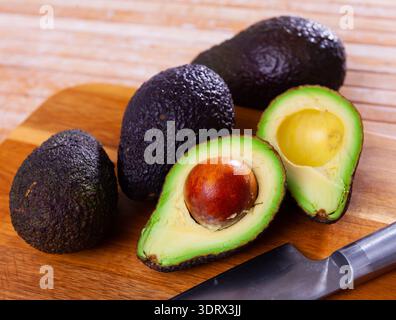 Whole and halved avocados on wooden cutting board Stock Photo