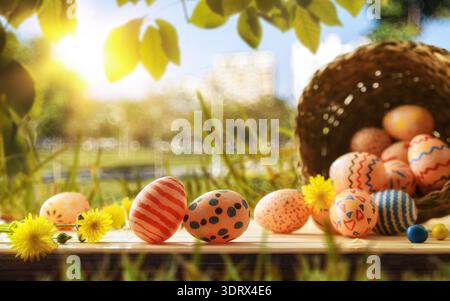Decorated Easter eggs on a wooden table with yellow flowers and a wicker basket in a sunny garden. Warm light and soft focus create a cheerful spring Stock Photo