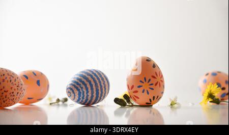 Colorful hand-painted Easter eggs with floral and striped patterns on a white reflective surface, decorated with small spring flowers in a minimalist Stock Photo