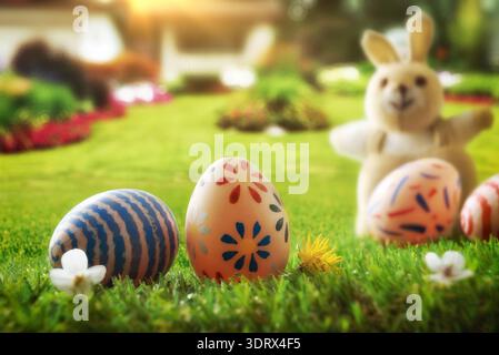 Colorful painted Easter eggs on fresh green grass with a soft-focus bunny and sunny garden background, spring atmosphere, shallow depth of field. Stock Photo