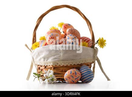 A wicker basket filled with hand-painted Easter eggs decorated with floral and polka dot patterns, surrounded by yellow flowers on a clean white backg Stock Photo