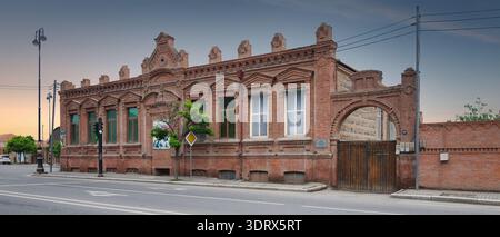 Ganja, Azerbaijan - May 13, 2024: Historic red brick building with ornate facade and arched entrance, featuring a Yasayis evi sign, on a quiet street under a clear sky Stock Photo