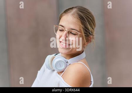 Young woman student smiling wearing headphones and glasses enjoying music Stock Photo