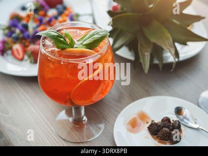 Colorful Drink With Fruit Garnish and Plates of Food on Wooden Table Stock Photo
