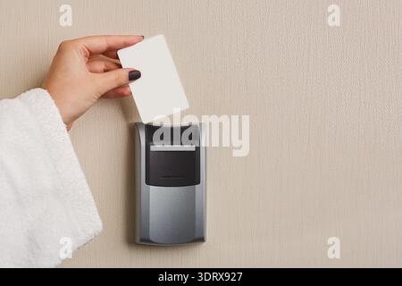 Hand Holding a Key Card Near a Card Reader on a Wall in a Hotel Room Setting Stock Photo
