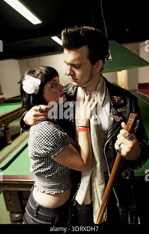 Young couple embracing beside a pool table, the man hugging the woman while he holds a pool cue. Stock Photo