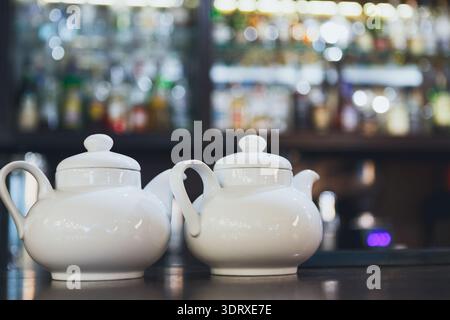 Collection of White Teapots on a Bar Counter With Blurred Background of Drinks and Bottles Stock Photo