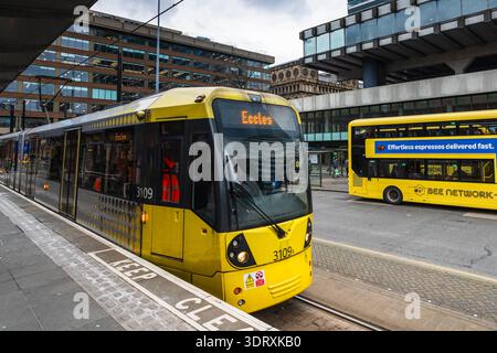 A bright yellow Bee Network Metrolink tram arriving at a station platform in Manchester with a yellow double-decker bus in the background on 18 Februa Stock Photo