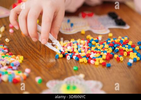 Child hand sorting thermomosaic ironing beads fuse beads on wooden table close up Stock Photo