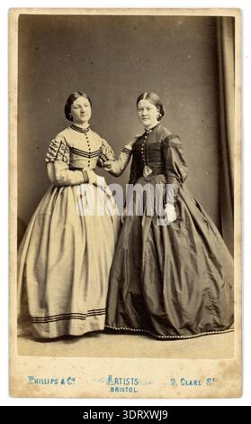 1860s pretty Victorian women, sisters, twins, cousins, beautiful dresses, crinoline style, smiling. 1860's ladies, lady, woman. Bristol UK.  Circa 1864 Stock Photo