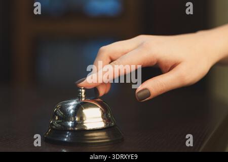 Hand Pressing a Service Bell at a Reception Desk in a Busy Setting Stock Photo