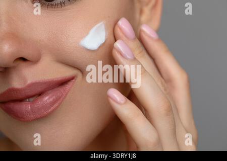 Woman with beautiful face touching healthy facial skin portrait. Beauty close up girl is applying a skincare cream. Hydration. Stock Photo