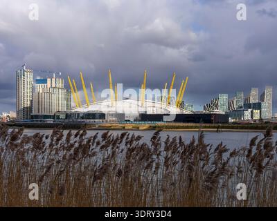 The O2 Arena seen from across the River Thames in east London, illuminated by sunlight beneath dark, cloudy skies. Stock Photo