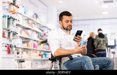 Disabled man using smartphone to take picture of skin care product in pharmacy Stock Photo