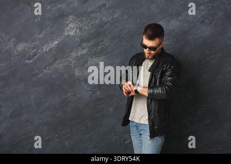 Man Checks Watch While Standing Against Dark Wall in Urban Setting Stock Photo