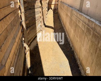 Narrow excavation trench between a wooden formwork wall and a newly poured concrete foundation wall at a residential construction site. The image show Stock Photo