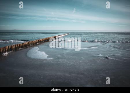 Minimalist winter seascape featuring a frozen Baltic Sea shoreline with smooth ice formations and a long wooden breakwater stretching into the horizon Stock Photo