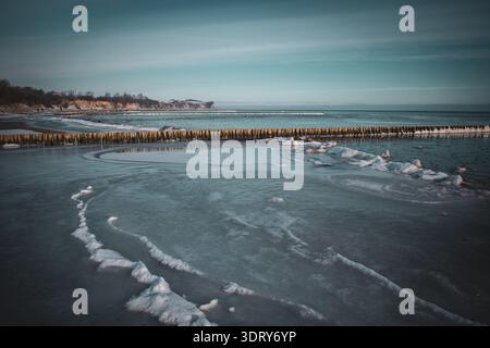 Minimalist winter seascape featuring a frozen Baltic Sea shoreline with smooth ice formations and a long wooden breakwater stretching into the horizon Stock Photo