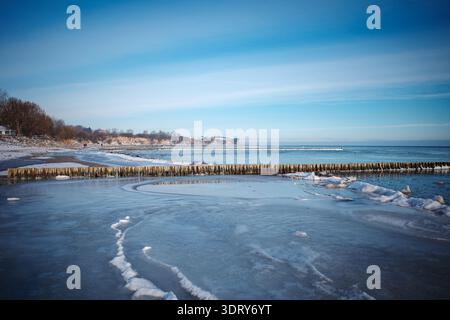 Minimalist winter seascape featuring a frozen Baltic Sea shoreline with smooth ice formations and a long wooden breakwater stretching into the horizon Stock Photo
