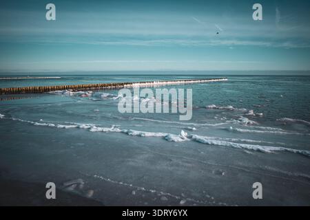 Minimalist winter seascape featuring a frozen Baltic Sea shoreline with smooth ice formations and a long wooden breakwater stretching into the horizon Stock Photo