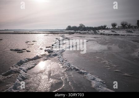 Moody winter sunset over a partially frozen Baltic Sea beach. The image captures icy shoreline formations, frozen sand patterns, and gentle waves unde Stock Photo