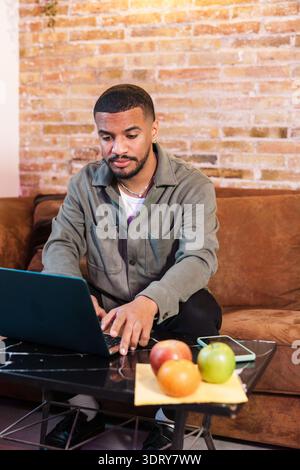 Focused young man working from home using laptop on the table with fruits Stock Photo