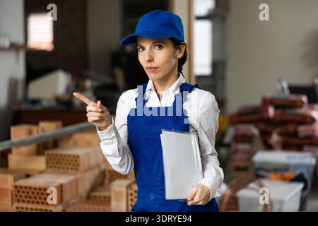 Female builder wearing overalls and cap posing at construction site, looking at camera Stock Photo