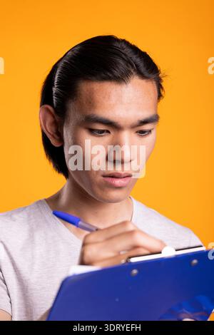 Determined male freelancer writes on clipboard, reviewing to do list. Focused man concentrates on goals and ideas, demonstrating organization, planning and motivated approach to personal productivity. Stock Photo