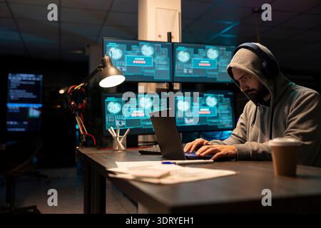 Adult male developer focusing intensely on encrypted network activity. Cybersecurity specialist types new software lines, detects threats and strengthens system defenses through diligent monitoring. Stock Photo
