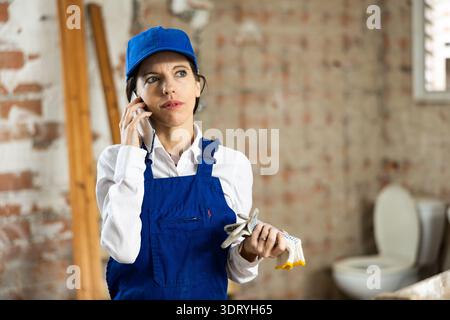 Female builder talking on phone with owner of building under renovation Stock Photo