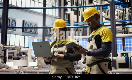 Team of smart factory mechanics working together to test systems, doing maintenance. Industry 4.0 plant teamworking repairmen inspecting equipment to identify glitches, doing brainstorming, camera A Stock Photo