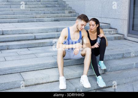 Couple Taking a Break While Exercising Together on Stone Steps in an Urban Setting Stock Photo