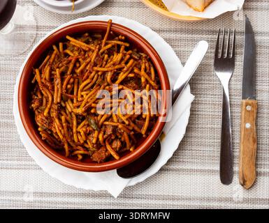There is portion of Chinese noodles with chicken and vegetables in deep clay plate Stock Photo
