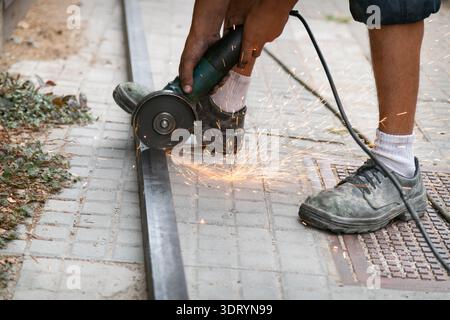 Worker using an angle grinder to cut a metal profile, creating sparks Stock Photo