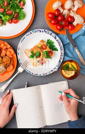 People Eating Lunch and Writing in the Notebook at the Table With Many Dishes of Food Stock Photo
