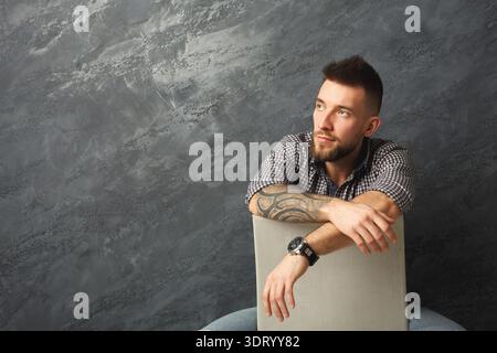 Man Rests Against a Soft Cushion in a Relaxed Setting With a Textured Wall in the Background Stock Photo
