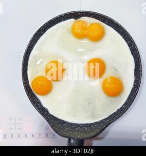 Delicious double-yolk eggs being fried in a non-stick pan, viewed from above, on a stovetop on induction cooker stove. Stock Photo