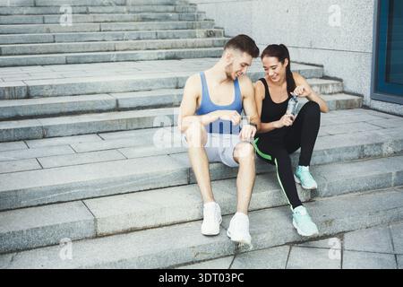 Couple Sits on Steps After Workout Sharing Snacks and Drinks While Relaxing Outside Stock Photo