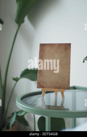 Blank canvas stands on green table near plants Stock Photo