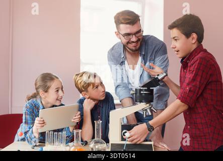 Students Learn About Science With Teacher Using Microscope and Equipment in Classroom Setting Stock Photo