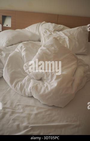 Blankets and pillows are disheveled on a bed in morning light Stock Photo