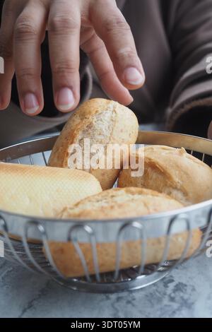 Hand reaching for bread rolls in a bowl on a table Stock Photo