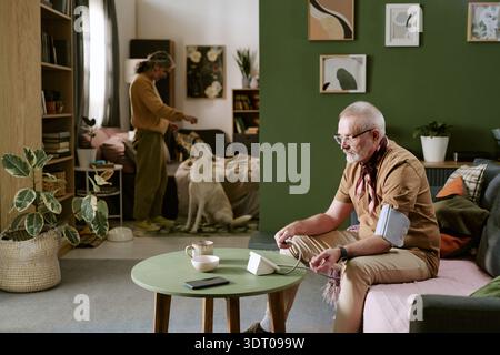 Senior Caucasian Man Measuring Blood Pressure While Sitting in Living Room Stock Photo