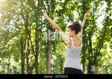 Young Woman Enjoying a Sunny Day in a Park While Posing With Joy and Energy Among the Trees Stock Photo