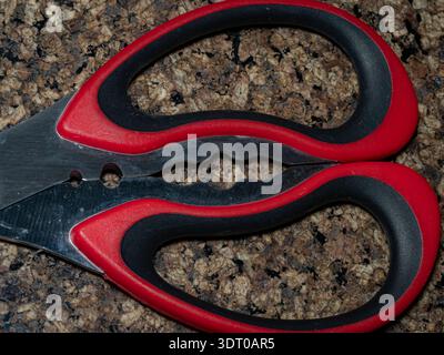 Close-up of red and black scissors on granite countertop, symbolizing household tools, safety, and craftsmanship Stock Photo