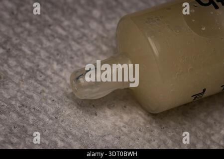 Macro close-up of a plastic dispenser bottle nozzle with bubble-filled liquid on a textured surface, showing product detail Stock Photo